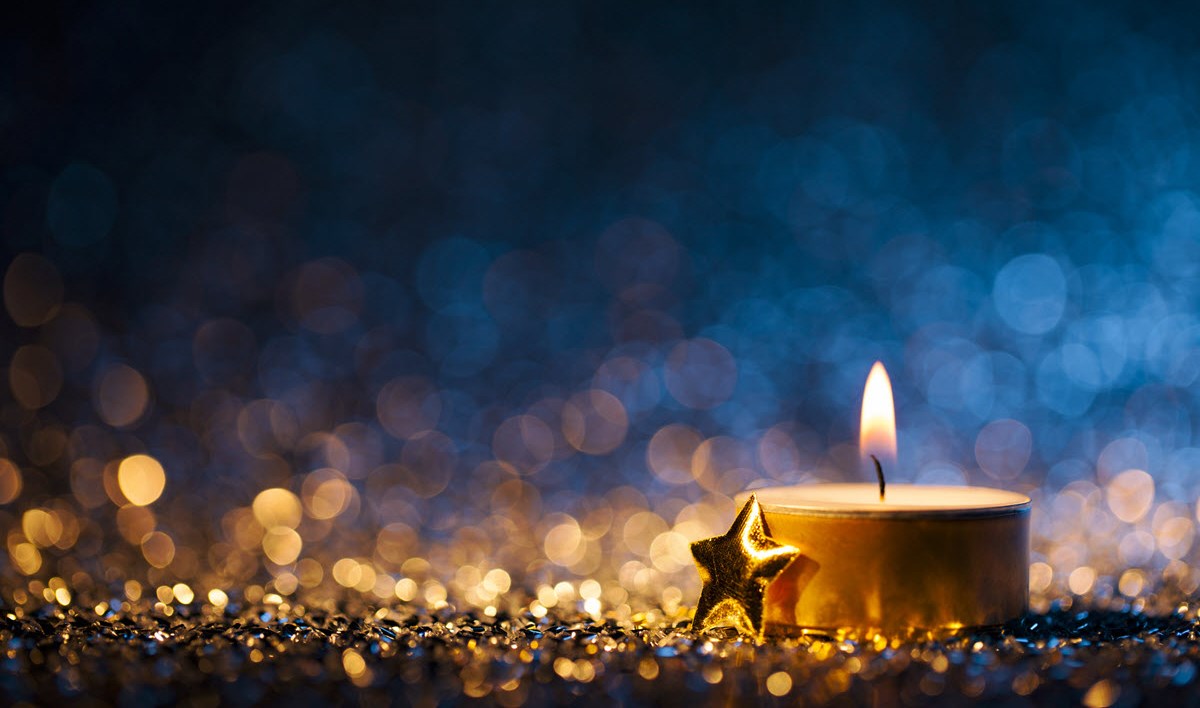 A close-up of a lit tea candle featured against a blue and gold backdrop, signifying the magic of the festive season.