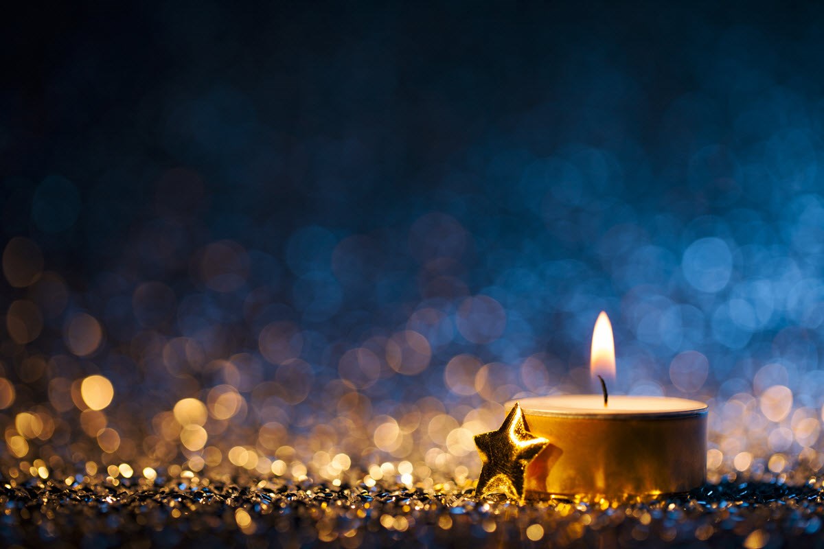 A close-up of a lit tea candle featured against a blue and gold backdrop, signifying the magic of the festive season.