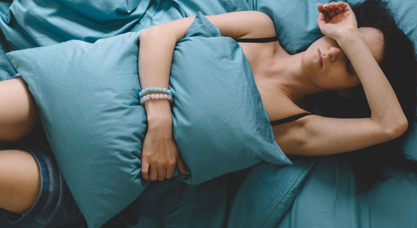 A woman lying on her bed covering her eyes with her arm in frustration because of the constraints placed on her by her chronic illness