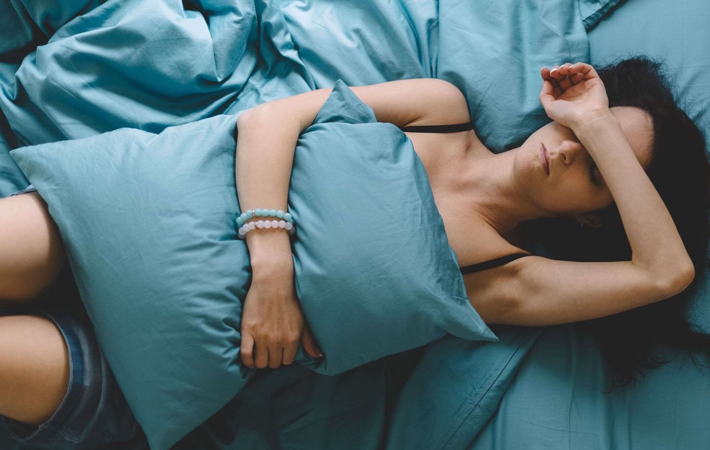 A woman lying on her bed covering her eyes with her arm in frustration because of the constraints placed on her by her chronic illness