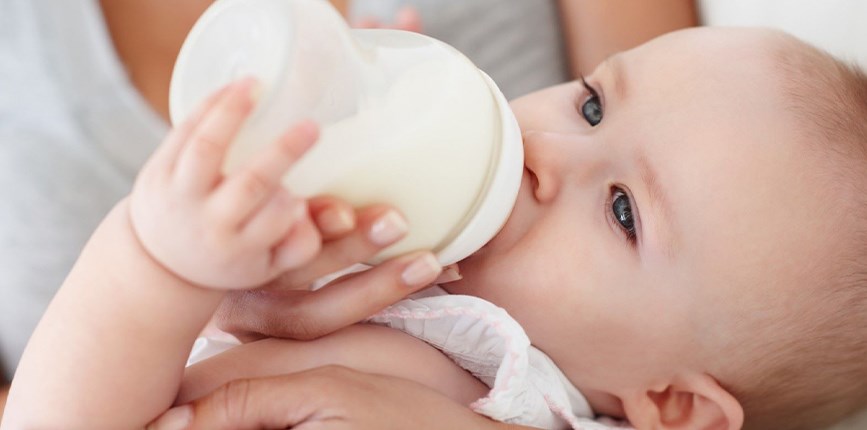 A mother holding her baby as they feed from a bottle.