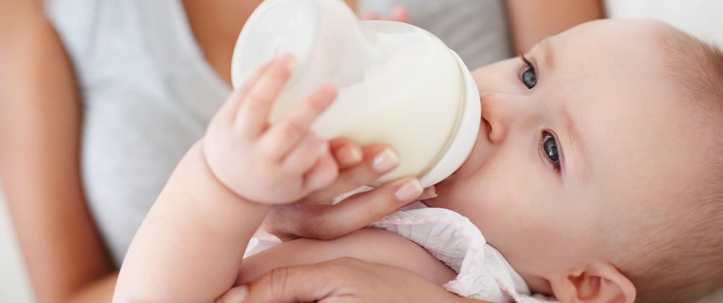 A mother holding her baby as they feed from a bottle.