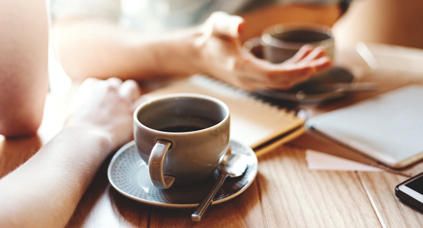 Close up of two people’s hands and two cups of coffee, showing two people in a therapeutic conversation.