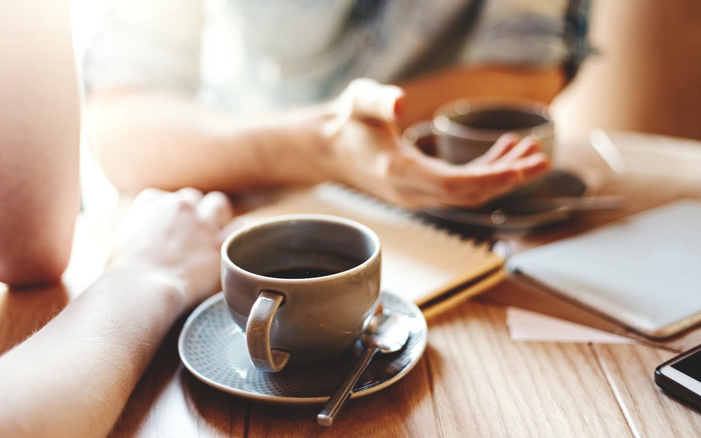 Close up of two people’s hands and two cups of coffee, showing two people in a therapeutic conversation.