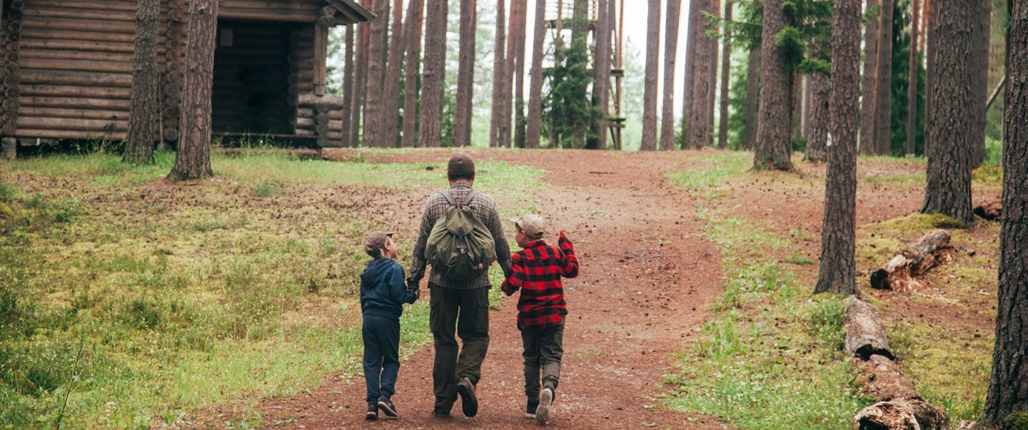 Dad holds hands with children as they walk in the woods