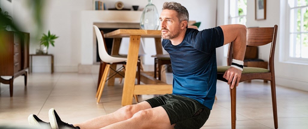 Male caregiver performing chair exercises in his kitchen to stay healthy 