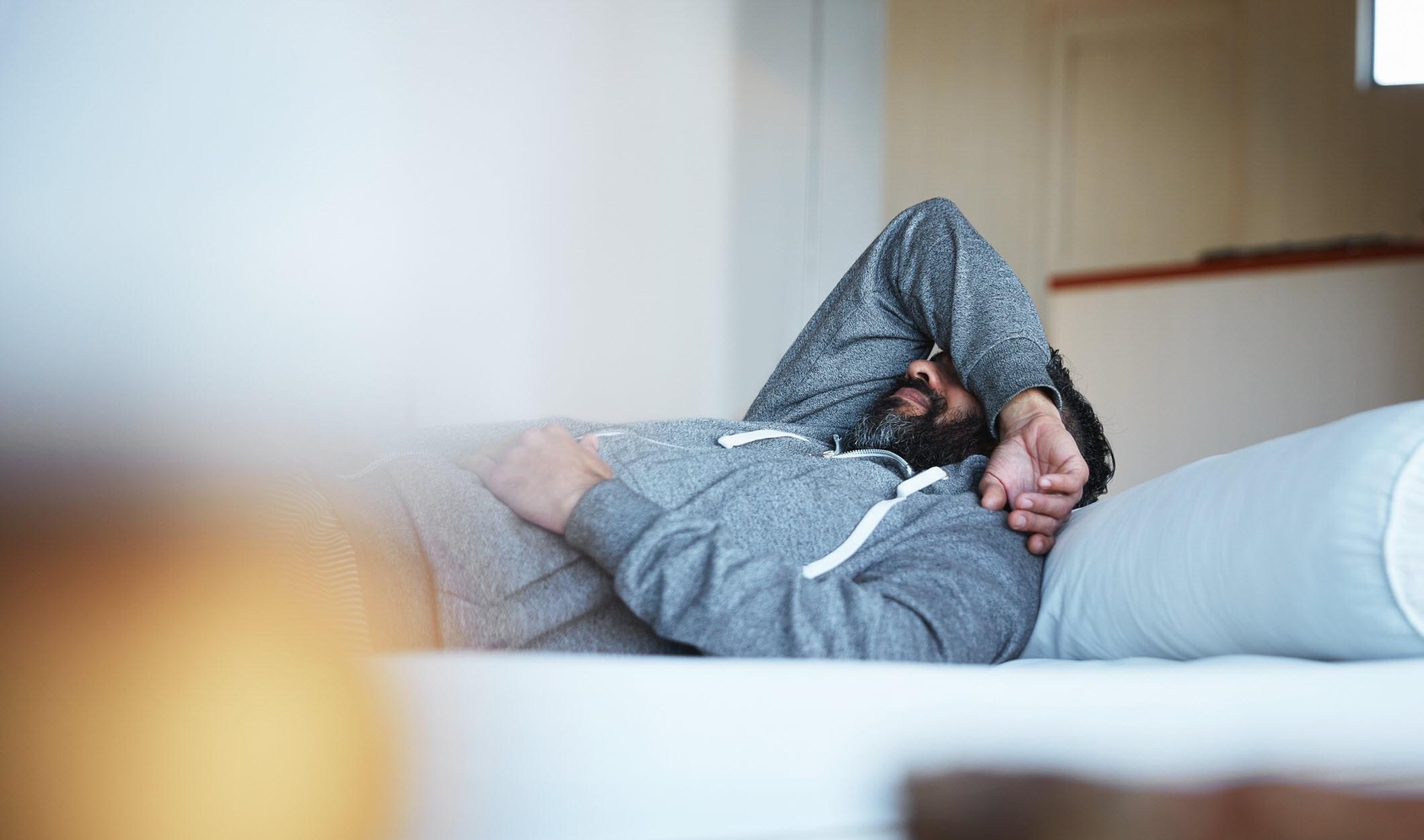 Man covering his face with arm on bed, struggling with depression.