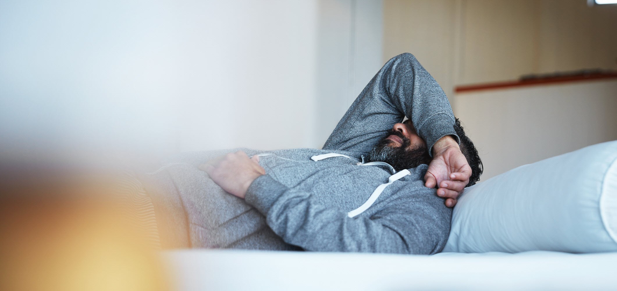 Man covering his face with arm on bed, struggling with depression.