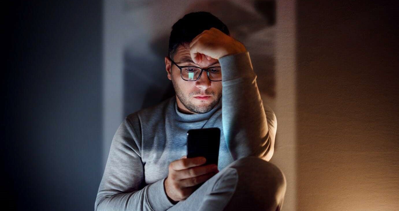 Man reading news app on his phone, depressed by negative headlines