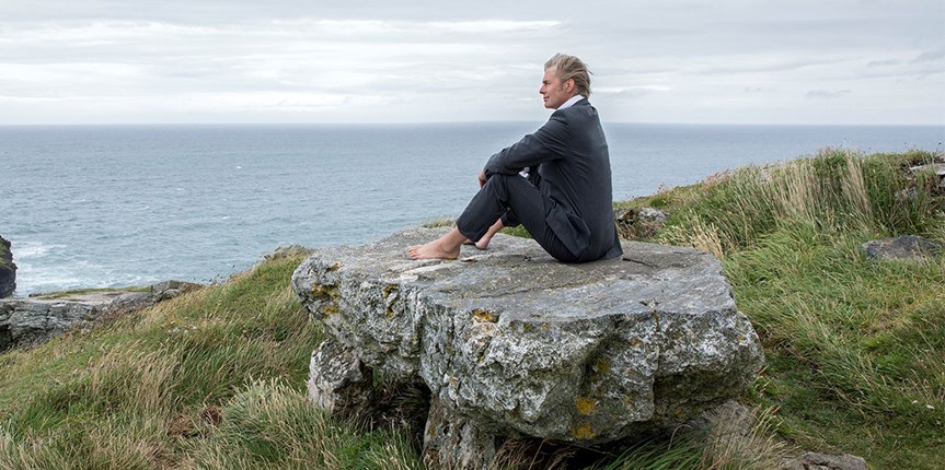 A man sitting on a boulder up a mountain after a long climb