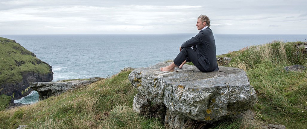 A man sitting on a boulder up a mountain after a long climb