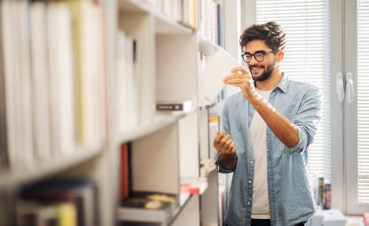 Man with ADHD cheerfully choosing his next book from the library