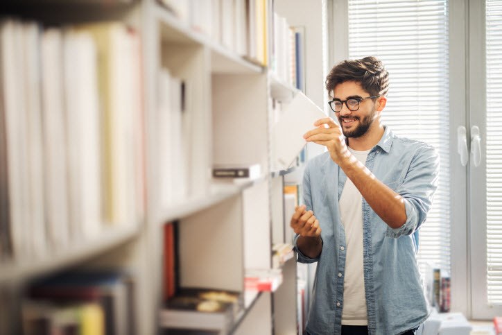 Man with ADHD cheerfully choosing his next book from the library