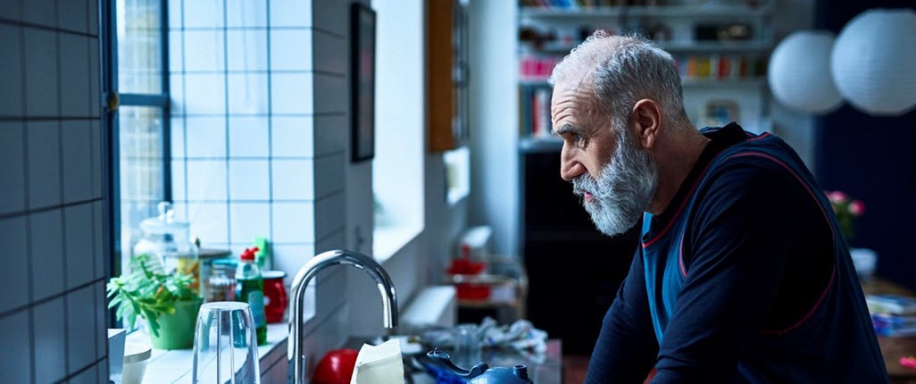 Stressed caregiver looks out of window as he considers all that lies ahead for him that day with his loved one and daughter