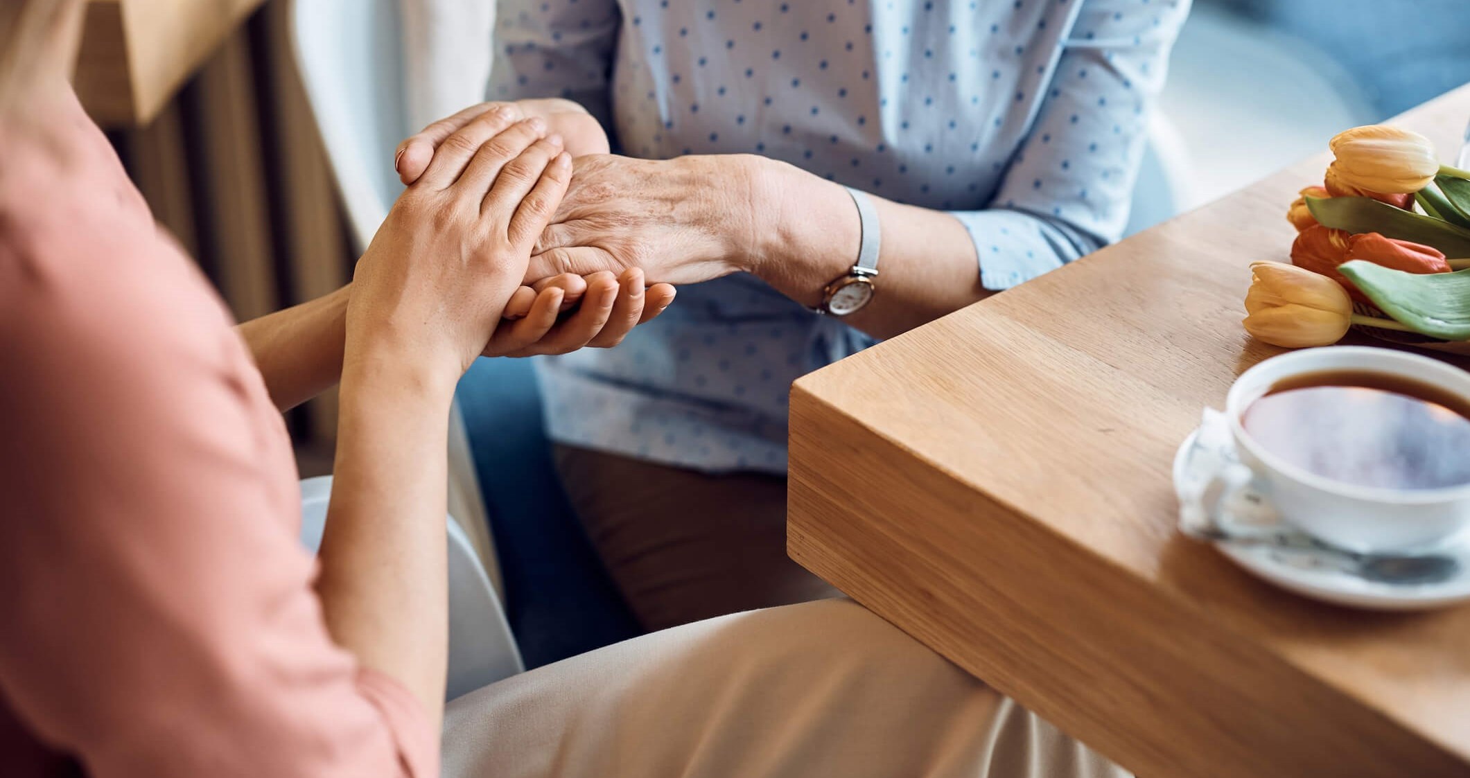 Daughter-caregiver tenderly holding elderly mother’s hand in cafe