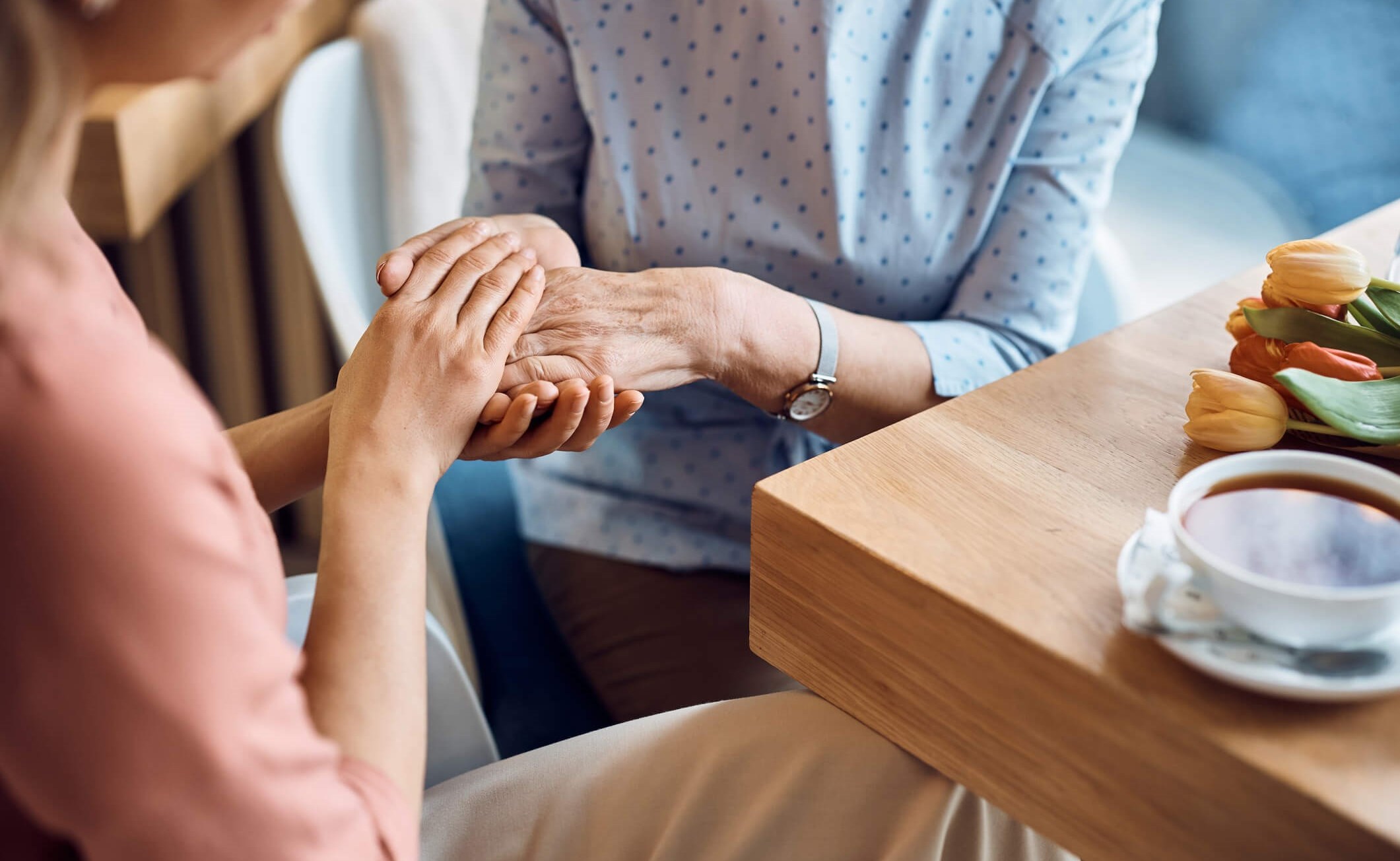 Daughter-caregiver tenderly holding elderly mother’s hand in cafe