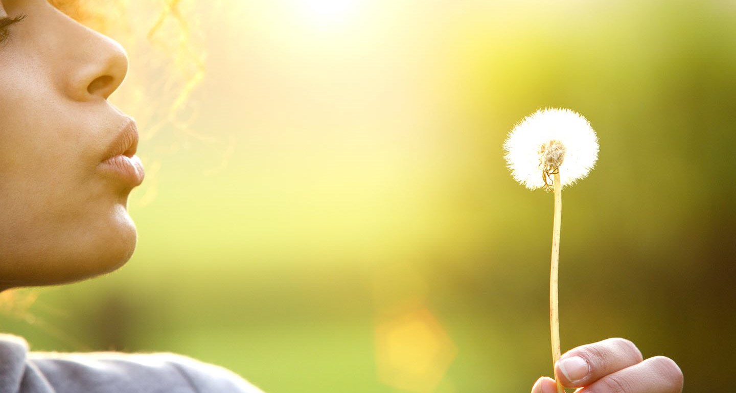 Woman blowing a dandelion in the summer air.