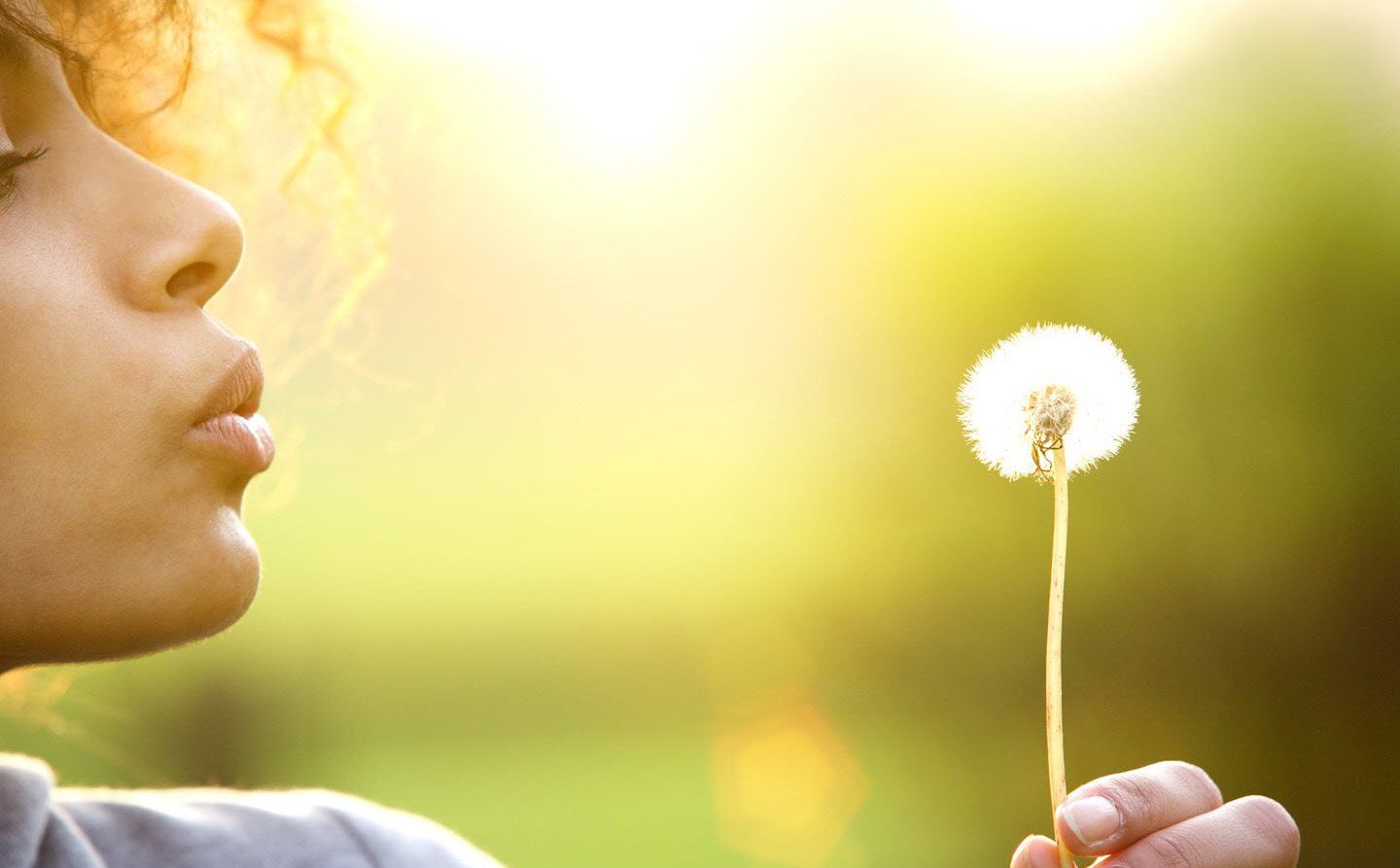 Woman blowing a dandelion in the summer air.