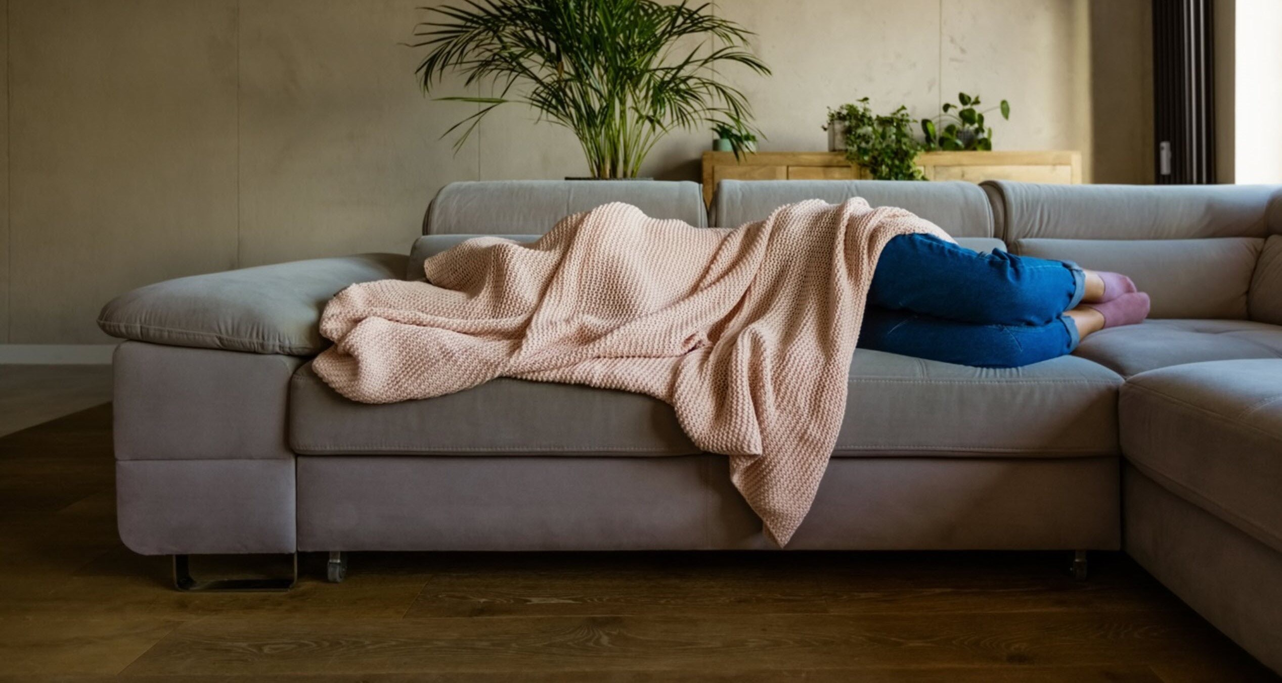 Woman hiding face under blanket on sofa struggling with migraine postdrome