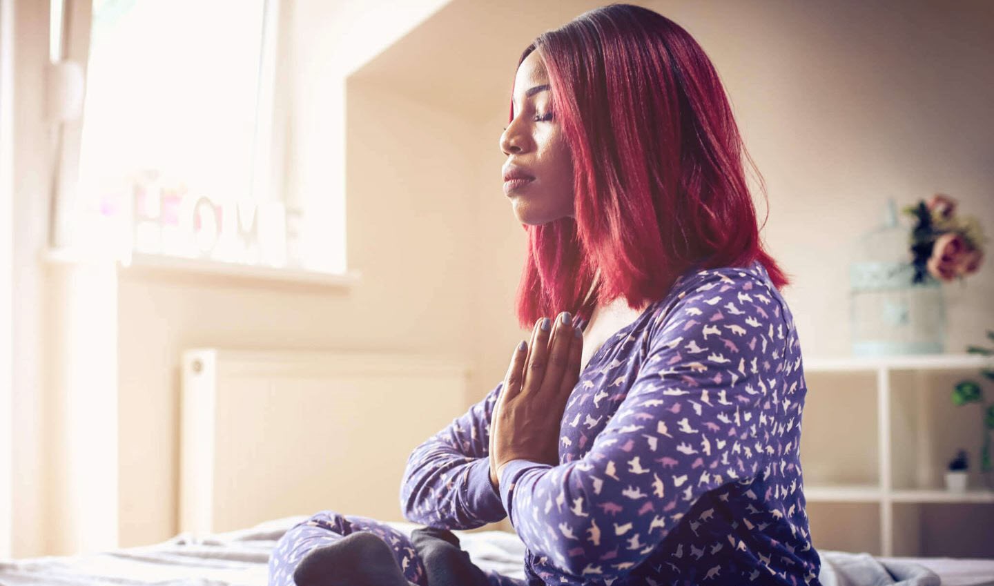 Woman meditating on her bed, gathering strength to face future migraine struggles