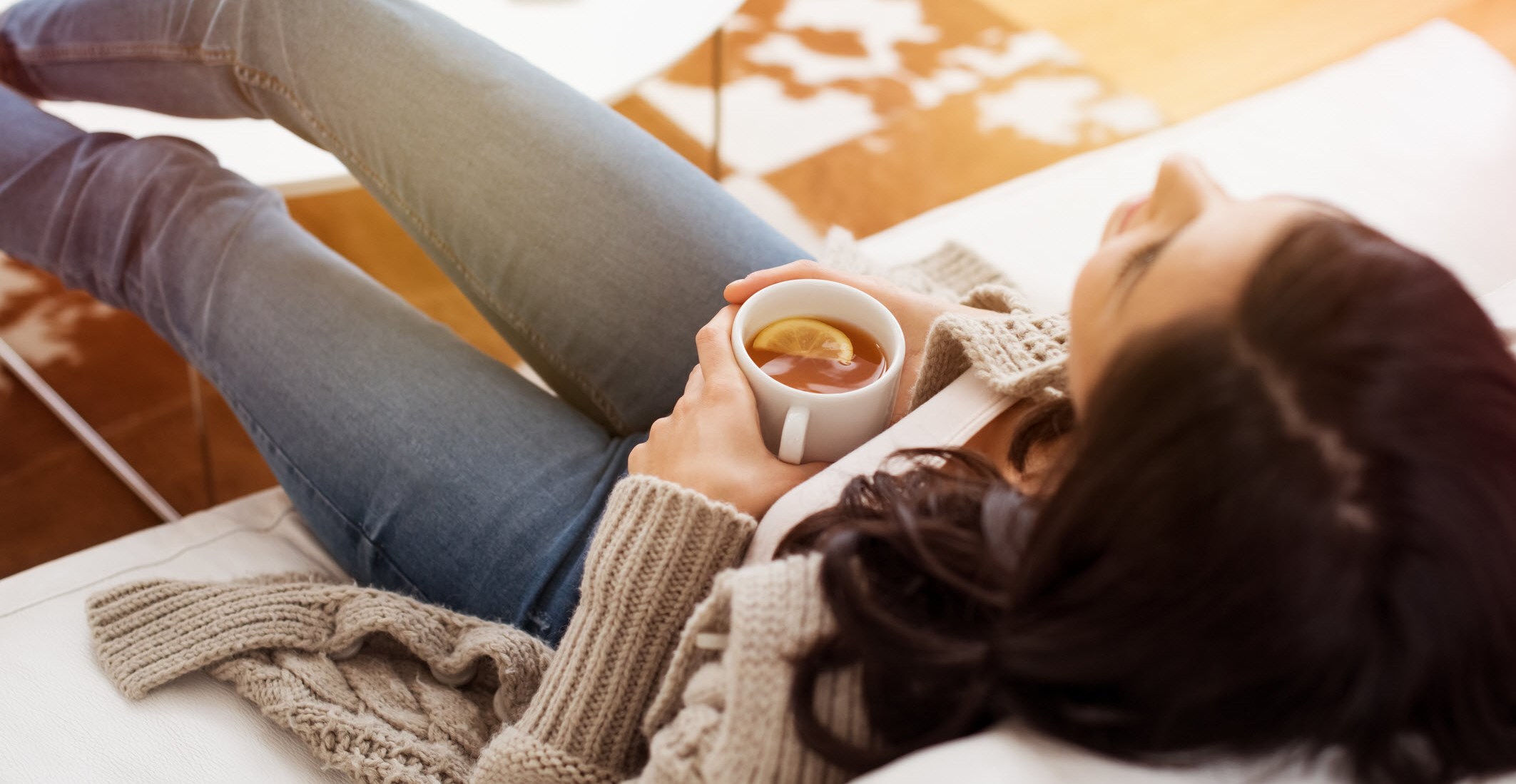 Woman relaxes on sofa with a cup of tea, staying calm in the days after an asthma flare-up.