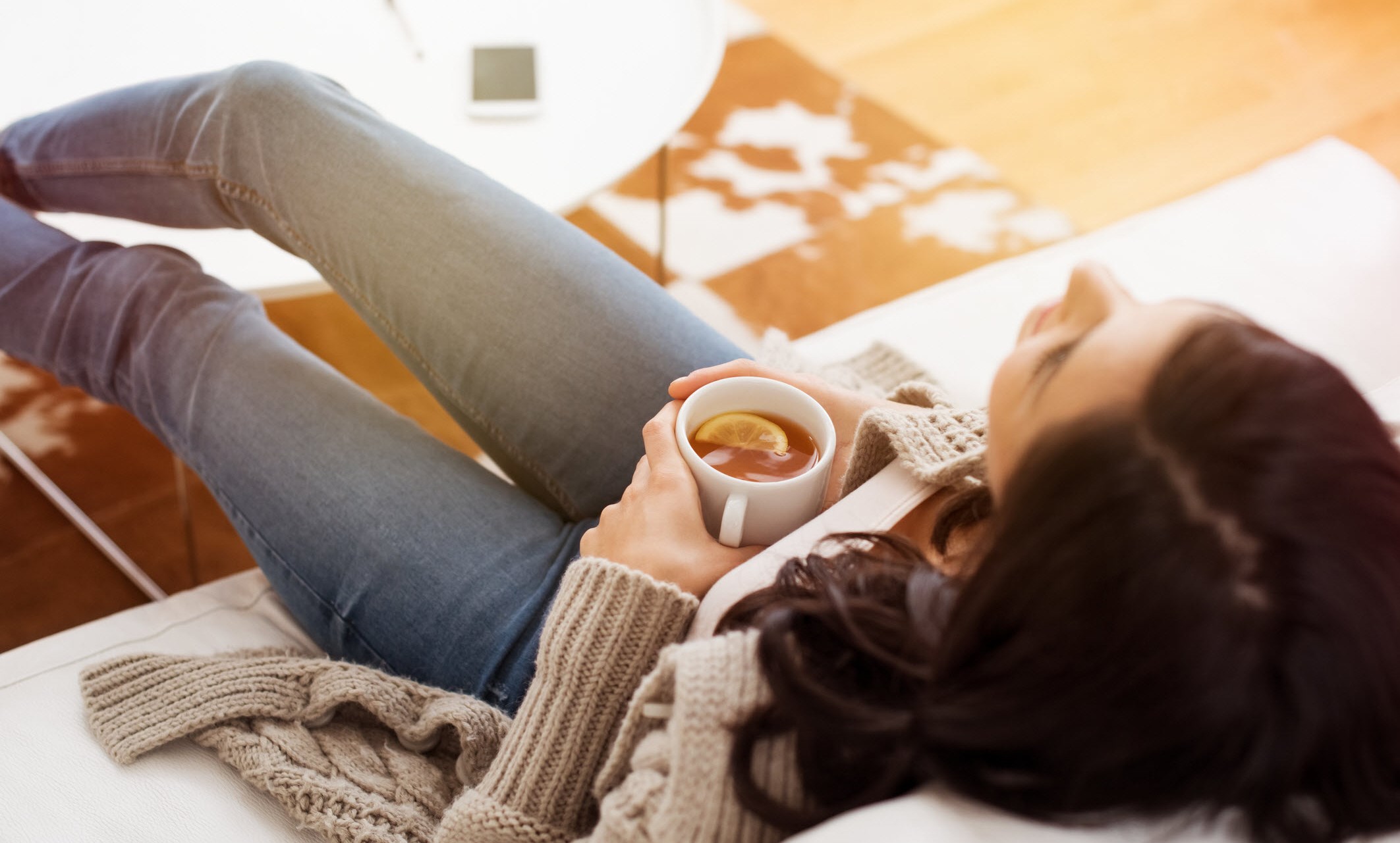 Woman relaxes on sofa with a cup of tea, staying calm in the days after an asthma flare-up.