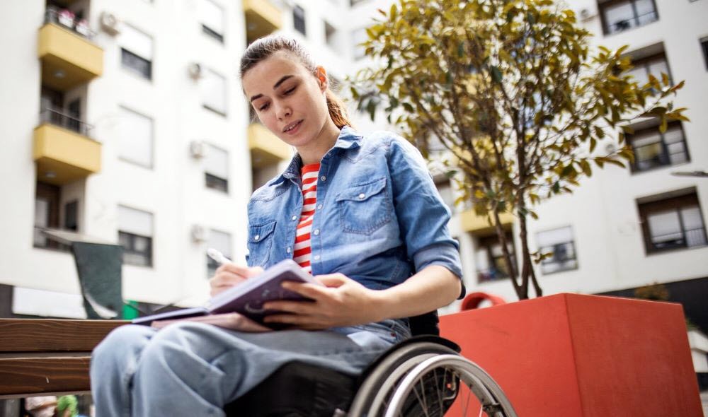 Woman sitting in wheelchair outside writing therapeutic poetry about migraine