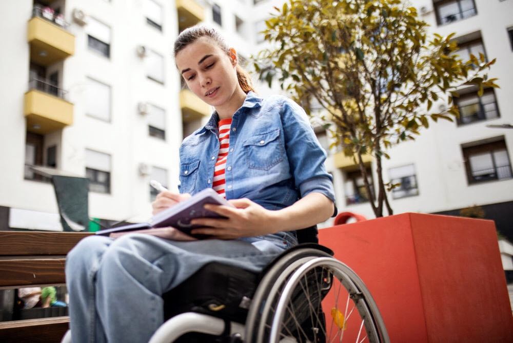 Woman sitting in wheelchair outside writing therapeutic poetry about migraine