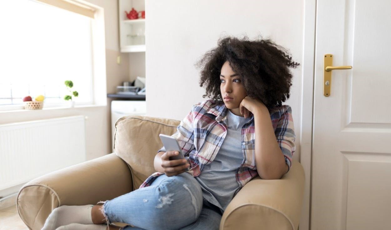 Depressed woman sitting on the couch with her phone in her hand