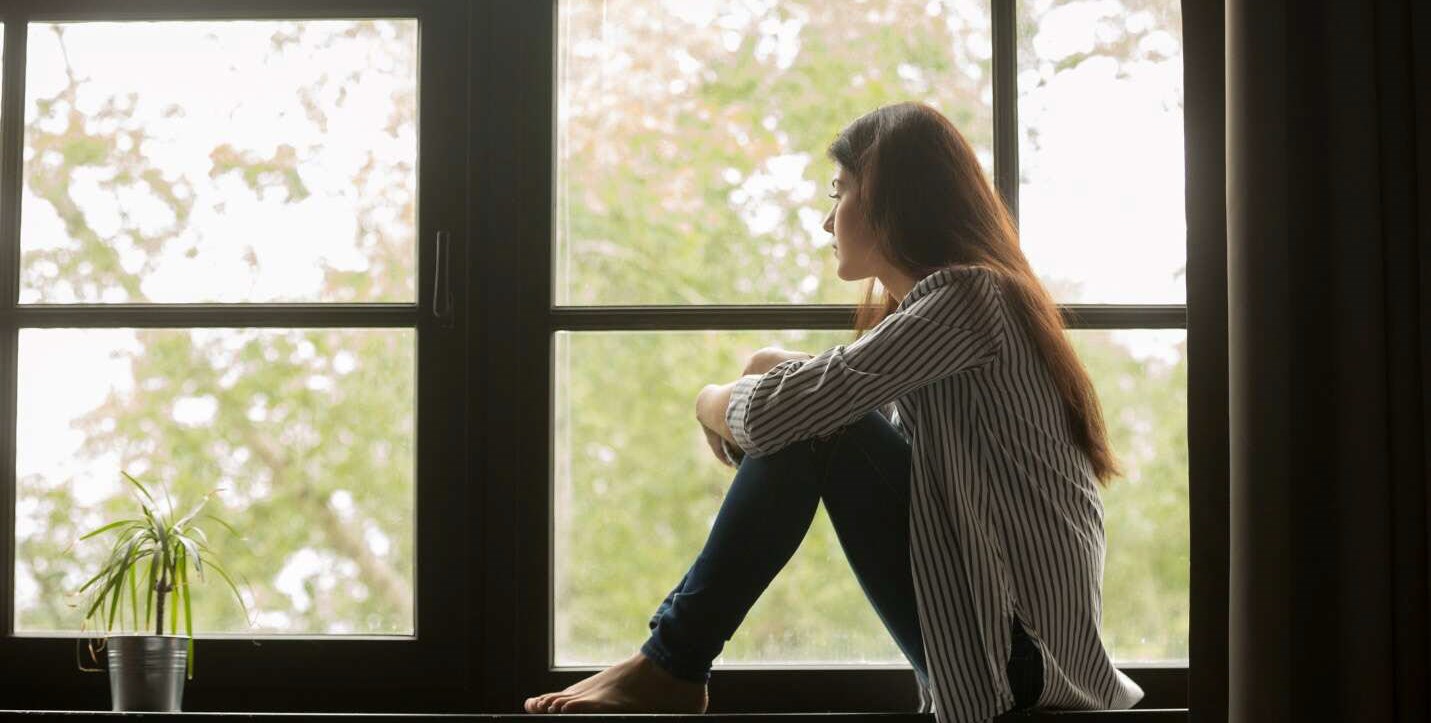 Woman sitting on windowsill, thinking about her anxiety triggers