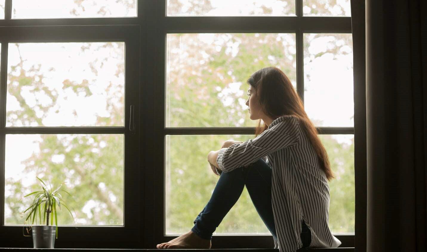 Woman sitting on windowsill, thinking about her anxiety triggers