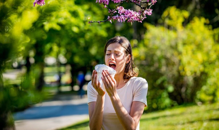 Woman sneezing due to pollen allergies under a blossom tree