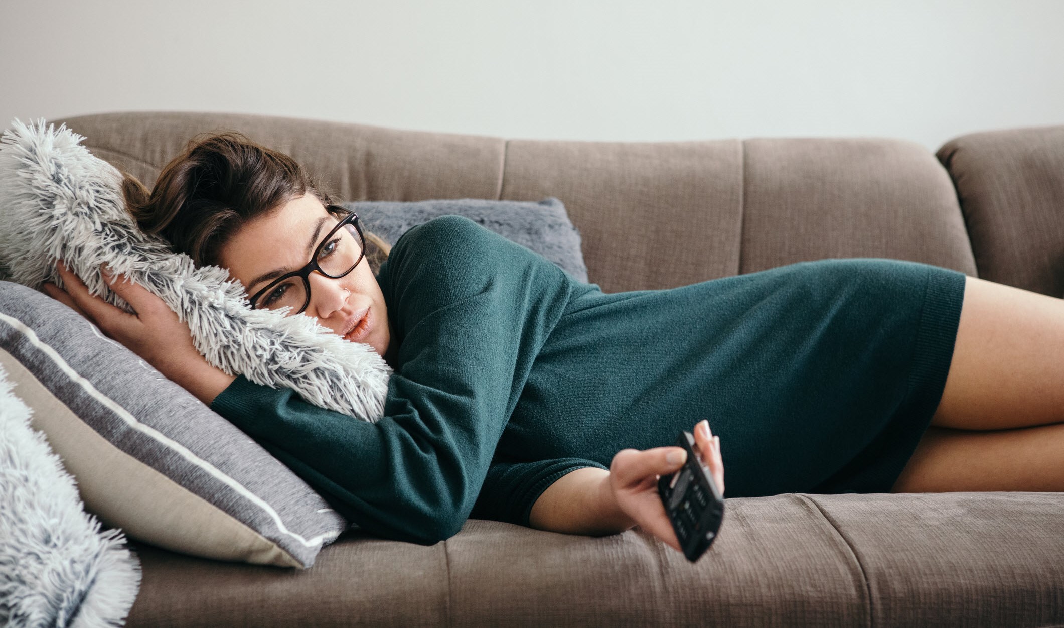 Woman watching TV lying on the coutch wih migraine