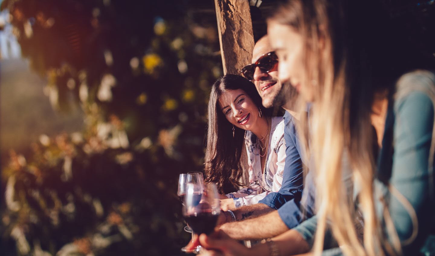 Woman with asthma drinking red wine with friends outside as the sun sets.