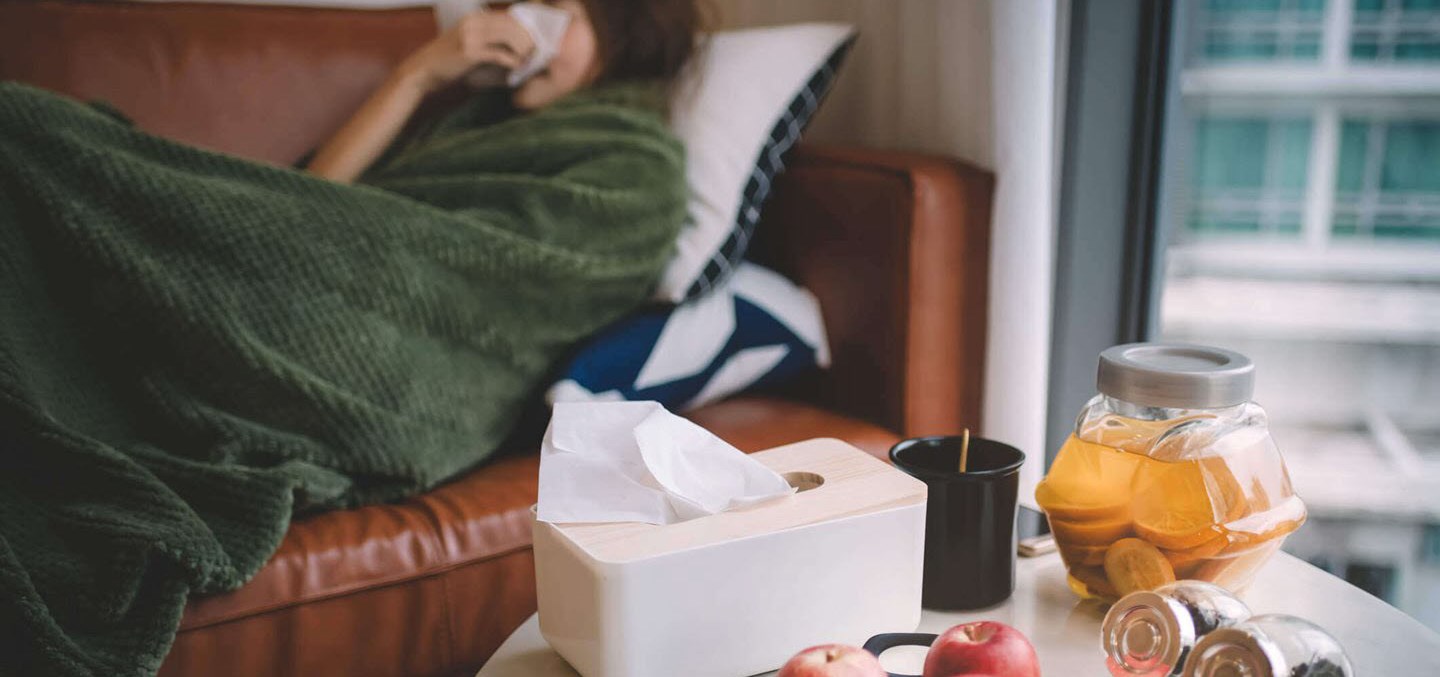 Woman with flu lying on her couch and blowing her nose with a tissue