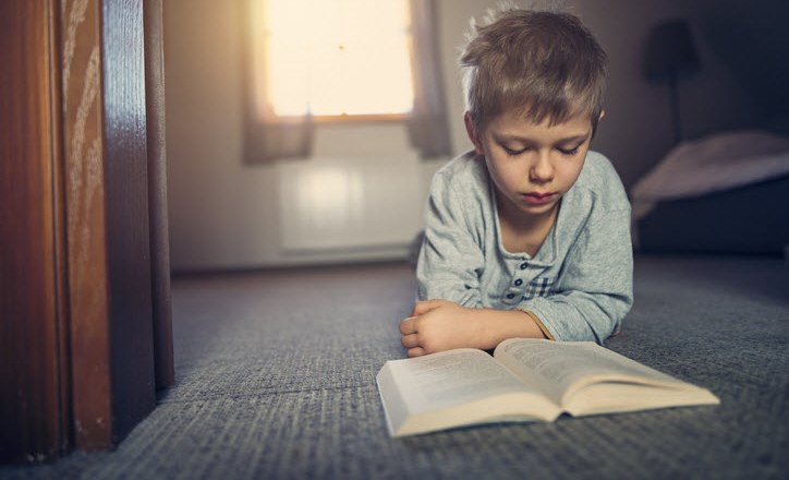 Young boy pouring over a book as his asthma can stop him from playing outside