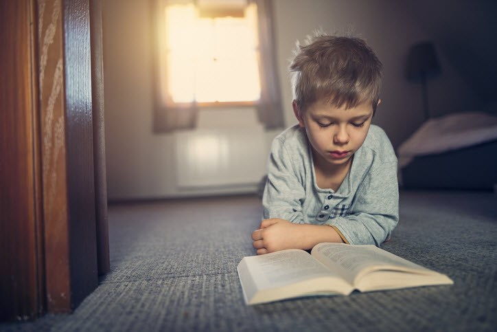 Young boy pouring over a book as his asthma can stop him from playing outside