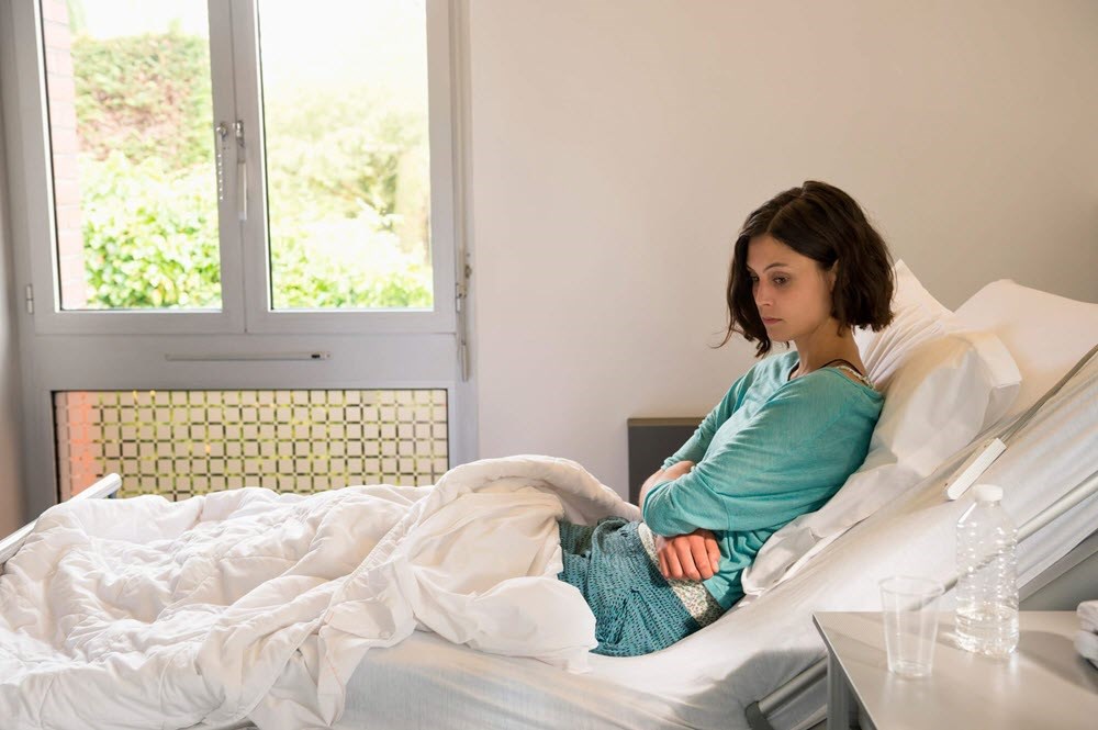 Young woman in hospital bed thinking about difficult health decisions 