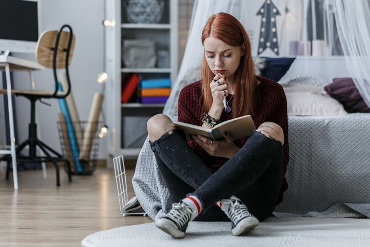 A young woman with chronic migraine sitting on the floor and browsing through a journal