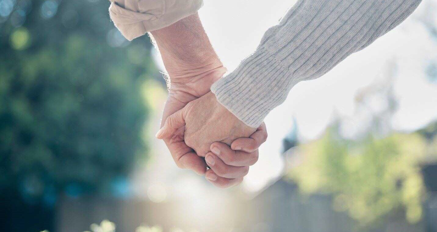 Mature couple united and holding hands, despite the strains of living with Huntington’s disease.