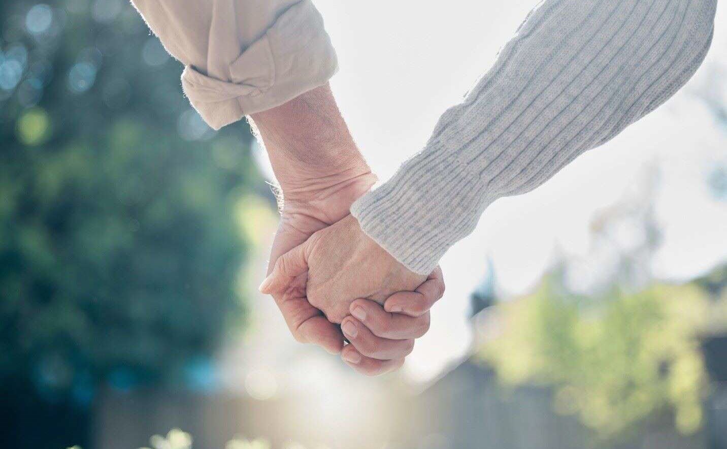 Mature couple united and holding hands, despite the strains of living with Huntington’s disease.