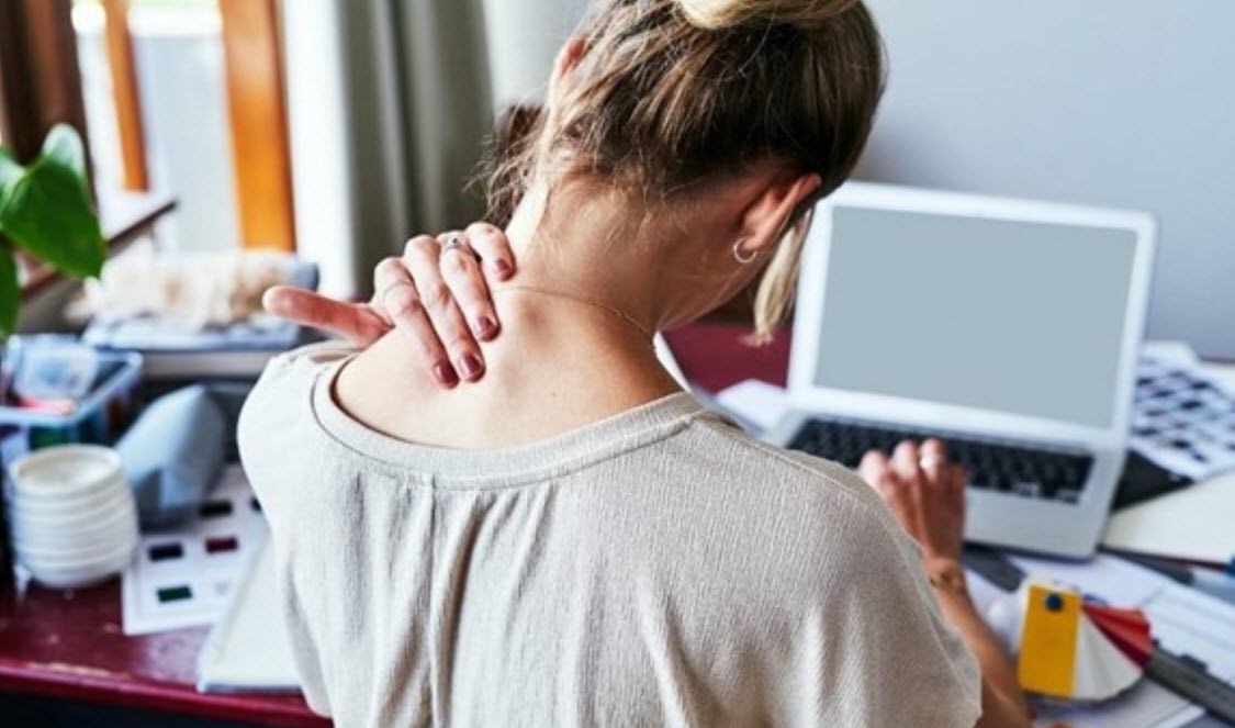 Woman at desk massages her neck to ease her pain and tension