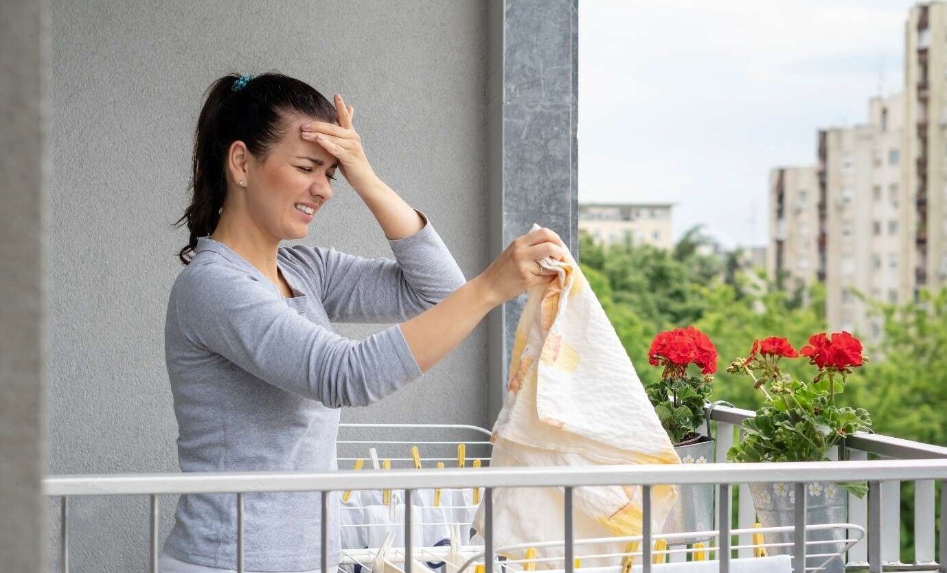 Woman on balcony struggling with migraine headache from ponytail as she hangs her laundry