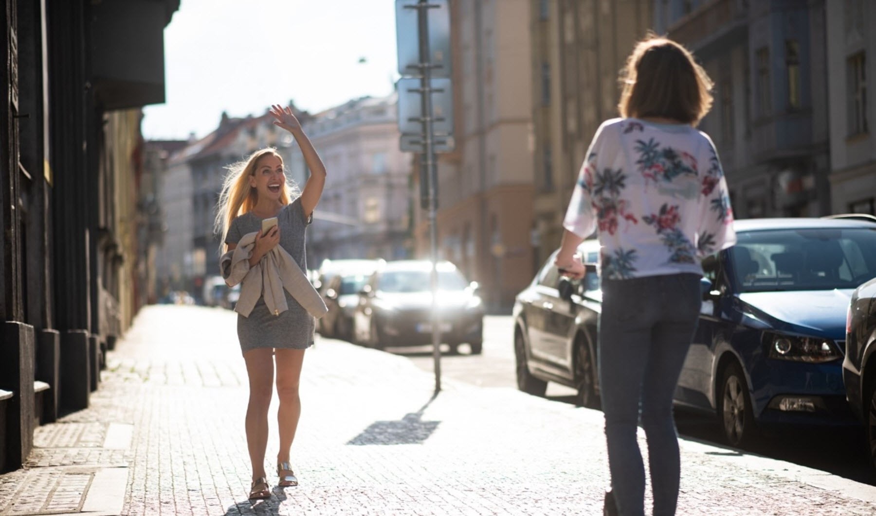 Female friends greet each other on the street one being enthusiastic the other more withdrawn