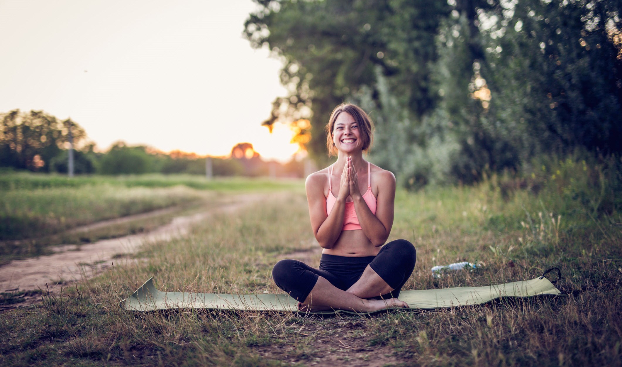 Woman smiling as she practices yoga in a field to help with chronic migraine