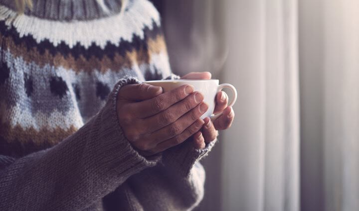 Woman with migraine holding a warming drink in the onset of a cold winter