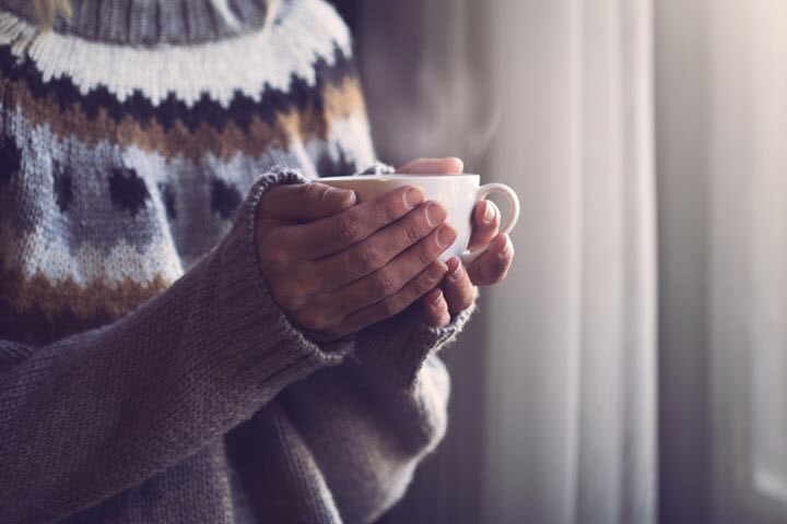 Woman with migraine holding a warming drink in the onset of a cold winter