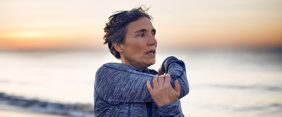 A woman on the beach at sunset stretches her arm